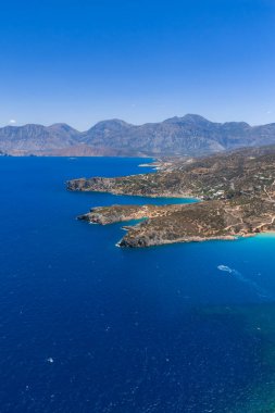 Yunanistan 'ın Girit kentindeki Voulisma Sahili' nin hava manzarasında turkuaz sular, kayalık yarımadalar, dolambaçlı yollar, dağınık bitki örtüsü ve uzak dağlar yer alıyor..