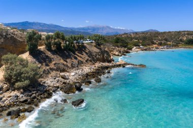 Yunanistan 'ın Girit kentindeki Voulisma Sahili' nin hava manzarasında turkuaz sular, kayalık uçurumlar, seyrek bitki örtüsü, güneş banyosu ve uzak engebeli dağlar görülüyor.
