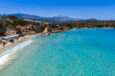 Yunanistan 'ın Girit kentindeki Voulisma Sahili' nin hava manzarasında turkuaz sular, şemsiyeli kumlu kıyılar, engebeli uçurumlar ve uzak dağlar yer alıyor..