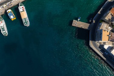 Girit 'teki Agios Nikolaos' un hava manzarası turkuaz suları, rıhtımlı tekneleri, kıvrımlı bir yolu ve kıyı şeridi yakınlarındaki ışıklı binaları gösteriyor..