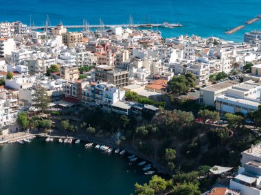 Girit 'in Agios Nikolaos kentinin havadan görünüşü, bir göl, pastel binalar, tekneli bir liman ve Akdeniz' in turkuaz sularını gösteriyor..