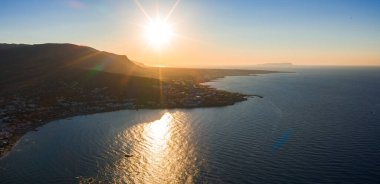 Gün batımında Girit Adası 'nın havadan görünüşü, dağlık bir kıyı şeridini, kıyıdaki küçük bir kasabayı ve altın ışığı yansıtan sakin denizi gösteriyor..