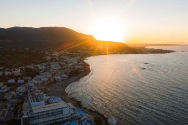 Gün batımında Stalida, Girit 'in havadan görünüşü, dağlık bir zemin, kıvrımlı kıyı şeridi, sakin deniz ve tepelere uzanan binalar..