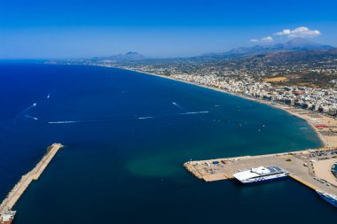 Yunanistan 'ın Girit kentindeki Rethymno kentinin havadan görünüşü, temiz bir gökyüzü altında yatı, dalgası, beyaz binaları ve dağları olan kumlu bir sahil, marinası bulunuyor..