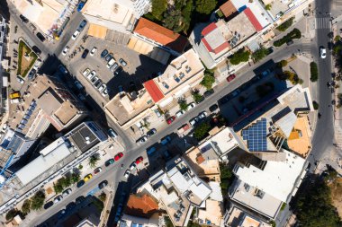 Girit, Rethymno 'nun hava görüntüsü, düz çatıları, güneş panelleri, park edilmiş arabalar, ağaçlık kaldırımlar ve sokak şebekesi olan açık renkli binaları gösteriyor..