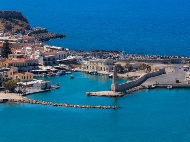 Yunanistan 'ın Girit kentindeki Rethymno kentinin hava manzarasında Venedik Limanı, ikonik deniz feneri, kırmızı kiremitli çatılar, turkuaz sular ve kayalık kıyı şeridi yer alıyor..