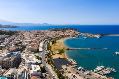 Girit, Rethymno 'nun havadan görünüşü, bir tepedeki Fortezza' yı, hilal şeklinde bir plajı, botlu bir marinayı ve arka planda Ege Denizi 'ni gösteriyor..