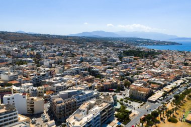 Açık renkli Akdeniz binaları, bir ağaç sıralı gezinti güvertesi ve açık mavi kıyı sularının yer aldığı Yunanistan 'ın Girit kentindeki Rethymno kentinin hava manzarası.