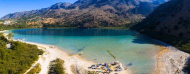Yunanistan 'ın Girit kentindeki Kournas Gölü' nün turkuaz suları tepelerle çevrilidir. Şemsiyeli kumsal, güneşli şezlonglar ve sahil boyunca yüzen tekneler..