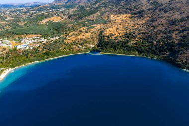 Yunanistan 'ın Girit kentindeki Kournas Gölü' nün hava manzarası, derin mavi sular, yemyeşil yemyeşil, kayalık arazi, kumlu kıyı şeridi ve yakınlardaki köyleri gösteriyor.