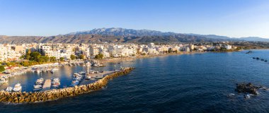 Yunanistan 'ın Girit kentindeki Chania kasabasının havadan görünüşü, kenetlenmiş tekneleri, taştan bir dalgakıranı, kıyı binaları ve güneşli dağları olan bir marinaya ev sahipliği yapıyor..