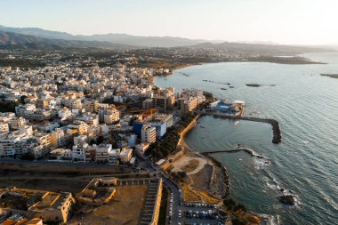 Girit, Chania 'nın havadan görünüşü, iskele, tarihi kalıntılar, yoğun binalar, yuvarlanan tepeler ve gün batımında Akdeniz' e sahip bir liman..