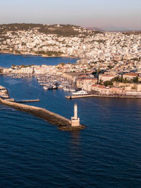 Venedik Limanı, ikonik deniz feneri, sakin sular, tarihi binalar ve altın bir günbatımı ışıltısının yer aldığı Girit 'teki Chania kasabasının hava manzarası..