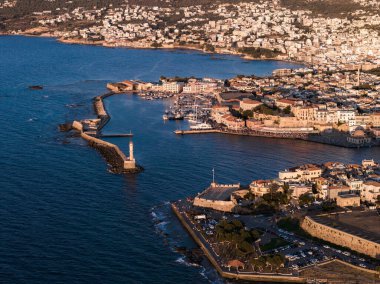 Venedik Limanı, ikonik deniz feneri, tarihi binalar ve şehrin üzerinde altın günbatımı renklerinin yer aldığı Chania, Girit, Yunanistan 'ın hava manzarası.