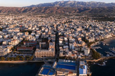 Günbatımında Girit, Yunanistan 'daki Chania' nın hava manzarası. Beyaz ve bej binalar, tekneli küçük bir liman ve mavi çatılı bir liman..
