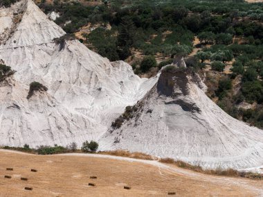 Potamida, Girit, Yunanistan 'daki Komolithi beyaz tepeleri, erozyon tarafından şekillendirilmiş konik oluşumlar, saman balyaları ve yemyeşil bitki örtüsü ile kuru bir alan..