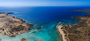 Yunanistan 'ın Girit kentindeki Elafonisi Sahili' nin hava manzarasında turkuaz sular, dar bir kumluk, kayalık çıkıntılar ve ufukta açık mavi bir gökyüzü görülüyor..