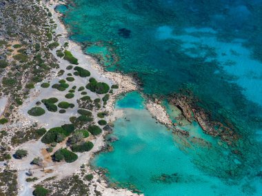 Yunanistan 'ın Girit kentindeki Elafonisi Sahili' nin havadan görünüşü, turkuaz ve derin mavi suları, engebeli kıyı şeridini ve kıyı boyunca uzanan yeşil alanları gösteriyor.