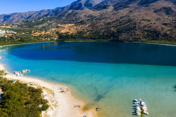 Yunanistan 'ın Girit kentindeki Kournas Gölü' nün havadan görünüşü turkuaz suları, tekneli kumlu bir sahil, engebeli tepeler ve dağınık uzak binaları gösteriyor..
