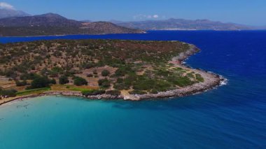 Girit 'teki Voulisma Sahili' nin havadan görünüşü kayalık kıyı şeridini, dalgalı derin mavi suları ve yavaş çekim yapan uzak tepeleri gösteriyor..