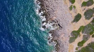 Girit, Voulisma Sahili yakınlarındaki kayalık kıyı şeridini gösteren hava manzarası canlı mavi sular ve yeşil yamalı engebeli arazi üzerinde geniş bir hareketlilik gösteriyor..