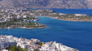 Agios Nikolaos, Girit 'in hava manzarası, beyaz ve pastel binaları gösteriyor, sakin mavi bir koy, etrafındaki tepeler ve aşamalı hareketler.