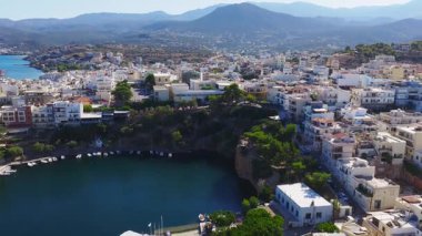 Beyaz ve pastel binaları, yemyeşil alanları, kıyı şeridini ve çevresindeki dağları gösteren yavaş ve süpürgen bir Agios Nikolaos, Girit tavası..