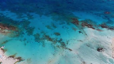 Girit 'teki Elafonisi Sahili' nin havadan görünüşü turkuaz suları, kayalık adalar ve kamera sahne üzerinde sorunsuz hareket ederken deniz yatağı desenleri gösteriyor..