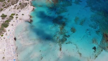 Girit 'teki Elafonisi Sahili' nin havadan görünüşü, pembe kum, turkuaz sular, plaj şemsiyeleri, güneş banyosu, küçük bir tekne ve hareket eden gölgeleri gösteriyor..