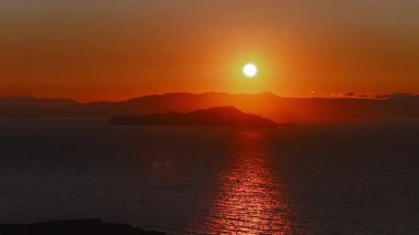 Yunanistan, Girit, Chania yakınlarında günbatımı manzarası. Güneş, denizlere turuncu ve kırmızı renkler saçar. Uzaktaki tepelerin ve adaların siluetleri....