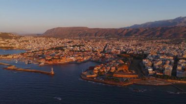 Günbatımında Yunanistan 'ın Girit kentindeki Chania kasabasının hava manzarası. Video beyaz ve pastel binaların, limanın ve Lefka Ori dağlarının üzerinden geçiyor..
