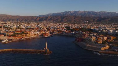 Venedik limanını, deniz fenerini, tarihi binaları ve dağları gösteren Chania, Girit 'in havadan görünüşü pürüzsüz insansız hava aracıyla altın bir günbatımı altında..