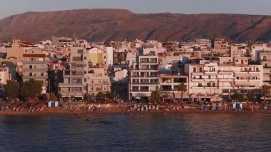 Girit, Chania 'nın altın saatindeki hava manzarası. Şemsiyeli ve güneşli sahiller, sakin sular, kasaba binaları ve güneşli dağlar..