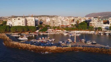 Chania şehrinin limanı, deniz feneri, şemsiyeli kumlu plaj ve güneşli bir günde tepeler ve dağlarla çevrili karışık mimari..