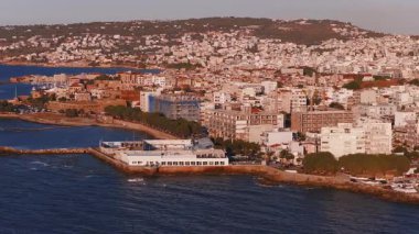 Yunanistan 'ın Girit kentindeki Chania kasabasının altın saat içindeki havadan görüntüsü. Beyaz ve pastel binalar, bir marina ve tepeler yavaş çekimle görülebilir..
