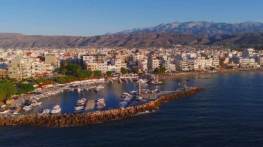 Yunanistan 'ın Girit kentindeki Chania kasabasının havadan görünüşü, açık mavi gökyüzü altında kayalıklar, kayalık çıkıntılar ve dağlarla dolu limanı gösteriyor..