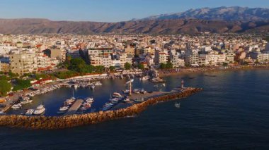 Yunanistan 'ın Girit kentindeki Chania kasabasının havadan görünüşü, beyaz ve pastel binaları, küçük tekneleri, berrak mavi suları ve engebeli dağları gösteren bir marina..