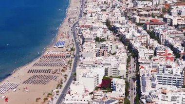 Girit, Rethymno 'nun havadan görünüşü, kumlu bir sahil, canlı mavi Akdeniz suları, kentsel mimari ve pürüzsüz hareket eden dağlık bir zemin gösteriyor..