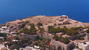 Yunanistan 'ın Girit kentindeki Fortezza hava sahasında taş duvarlar, yeşillik, kıyı yolu, park edilmiş arabalar ve Akdeniz görülüyor..