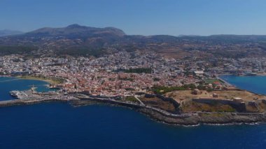Rethymno 'nun havadan görünüşü, Girit' te deniz feneri, eğri dalgalar, hareket eden tekneler, beyaz sahil binaları ve dağlık zemin.