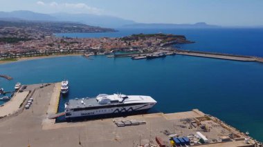 Girit, Rethymno 'nun havadan görünüşü, limanı feribot ve gemiyle gösteriyor, sakin mavi sular, yoğun binalar, yuvarlanan tepeler ve uzak dağlar..