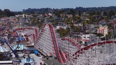 Santa Cruz Sahili 'ndeki dev hız treninin üzerinde renkli binalar, palmiye ağaçları ve güneşli bir tepe arkaplan var..