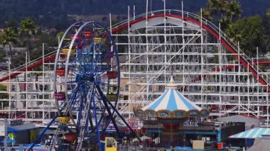 Güneşli bir günde, Santa Cruz, Kaliforniya 'da dev bir hız treninin, Amerikan bayrağının, palmiye ağaçlarının ve yerleşim alanlarının hava görüntüsü..