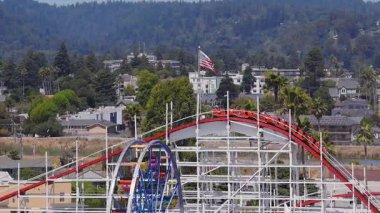 Kaliforniya 'daki Santa Cruz Sahili Boardwalk manzarası. Giant Dipper, hareket halindeki dönme dolap, atlıkarınca, kumlu sahil ve çevresindeki tepeler..