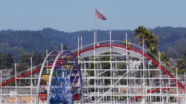 Santa Cruz, California 'nın havadan görünüşü, dev hız treni, dönme dolap, sallanan Amerikan bayrağı, yeşil tepeler ve palmiye ağaçları....