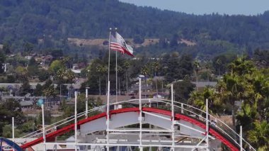 Santa Cruz, California 'nın havadan görünüşü, dev hız treni, dalgalanan bayraklar, renkli binalar, palmiye ağaçları ve yeşil tepeler.