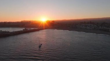 Santa Cruz, California 'nın hava manzarası, gün batımında iskele, park edilmiş arabalar, okyanus ve kasabanın silueti. Kamera sahne boyunca yavaş yavaş kayar..