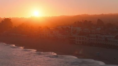 Santa Cruz, California 'nın havadan görünüşü, kıyı şeridini, rıhtımı ve şehir siluetini gösteriyor. Dalgalar ve günbatımının ışıkları hareket halinde..