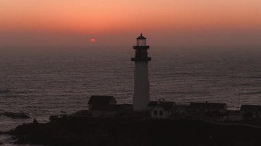 Güvercin Noktası Deniz feneri, günbatımında turuncu ve pembe bir gökyüzüne karşı duruyor. Arka planda okyanus ve hafif dalgalar, sakin bir hareket ekliyor..