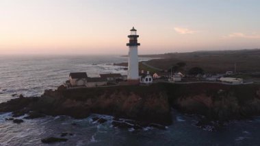 Güvercin Noktası Deniz feneri California 'da bir sahil uçurumunda okyanus dalgalarının altında duruyor. Gün batımında kamera hafifçe döner..